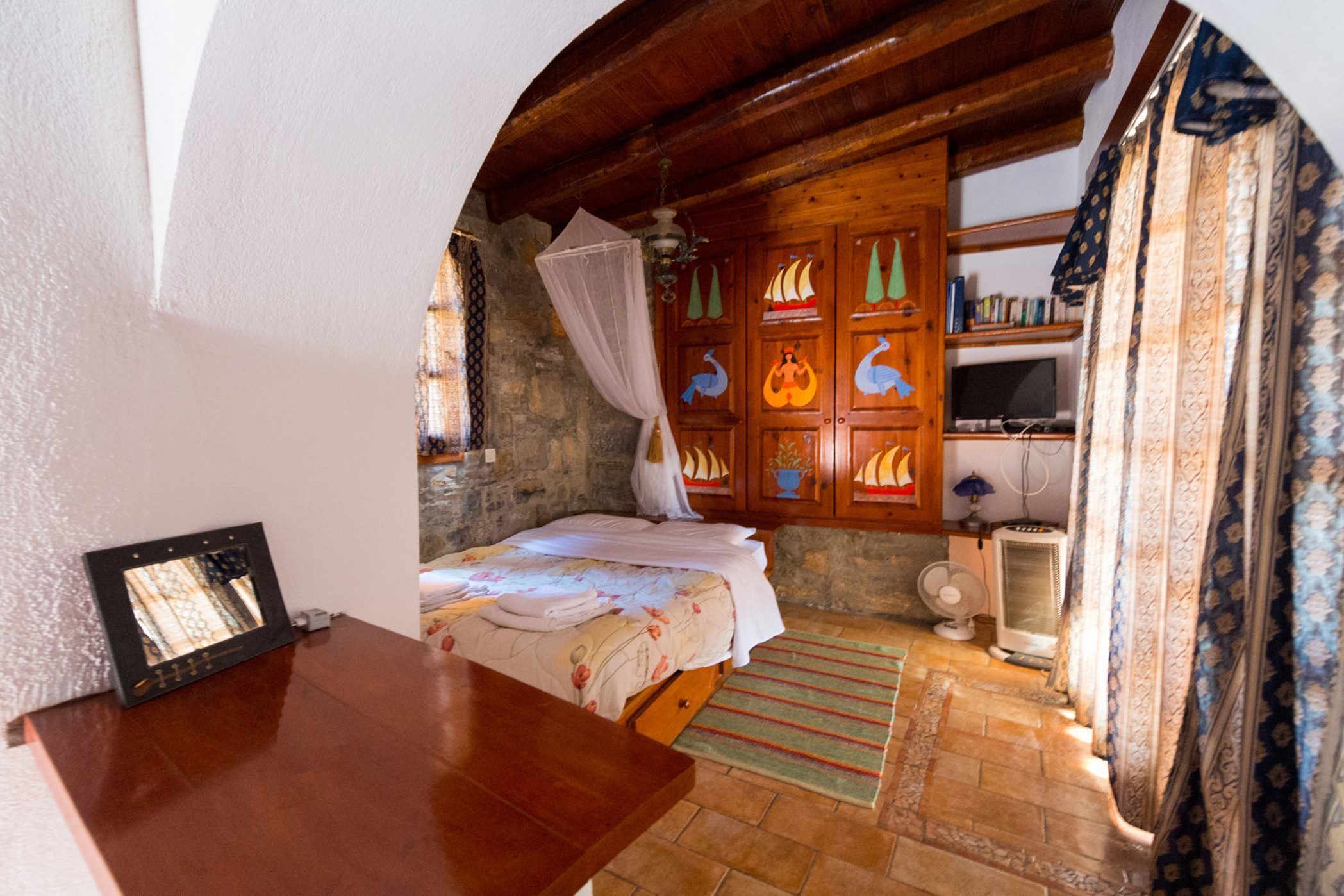 Una habitació acollidora amb un llit, armaris de fusta amb portes decoratives, una televisió i un ventilador.