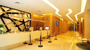 A modern hotel reception area with a reception desk, two monitors, and a seating area with a chair.