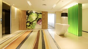 A modern hotel lobby with a striped carpet, a large abstract painting, a reception desk, and a green accent wall.