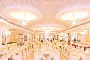 Uma sala de banquetes com mesas redondas, lustres e decoração em branco.