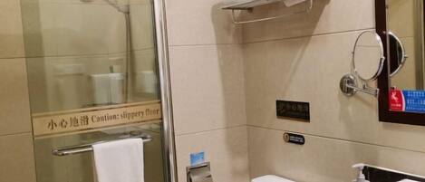 A hotel bathroom with a glass shower enclosure, a toilet, a sink, and a towel rack.