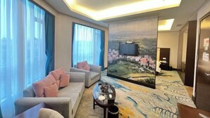 Une chambre d’hôtel avec une grande fenêtre, un canapé, une table basse et un tableau représentant un paysage urbain.