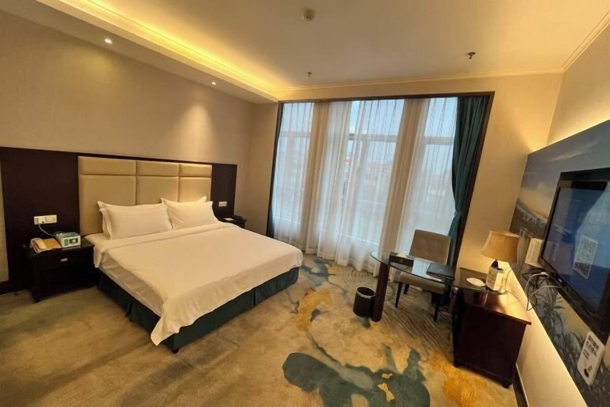 A hotel room with a large bed, a desk, a chair, a TV, and a window with curtains.