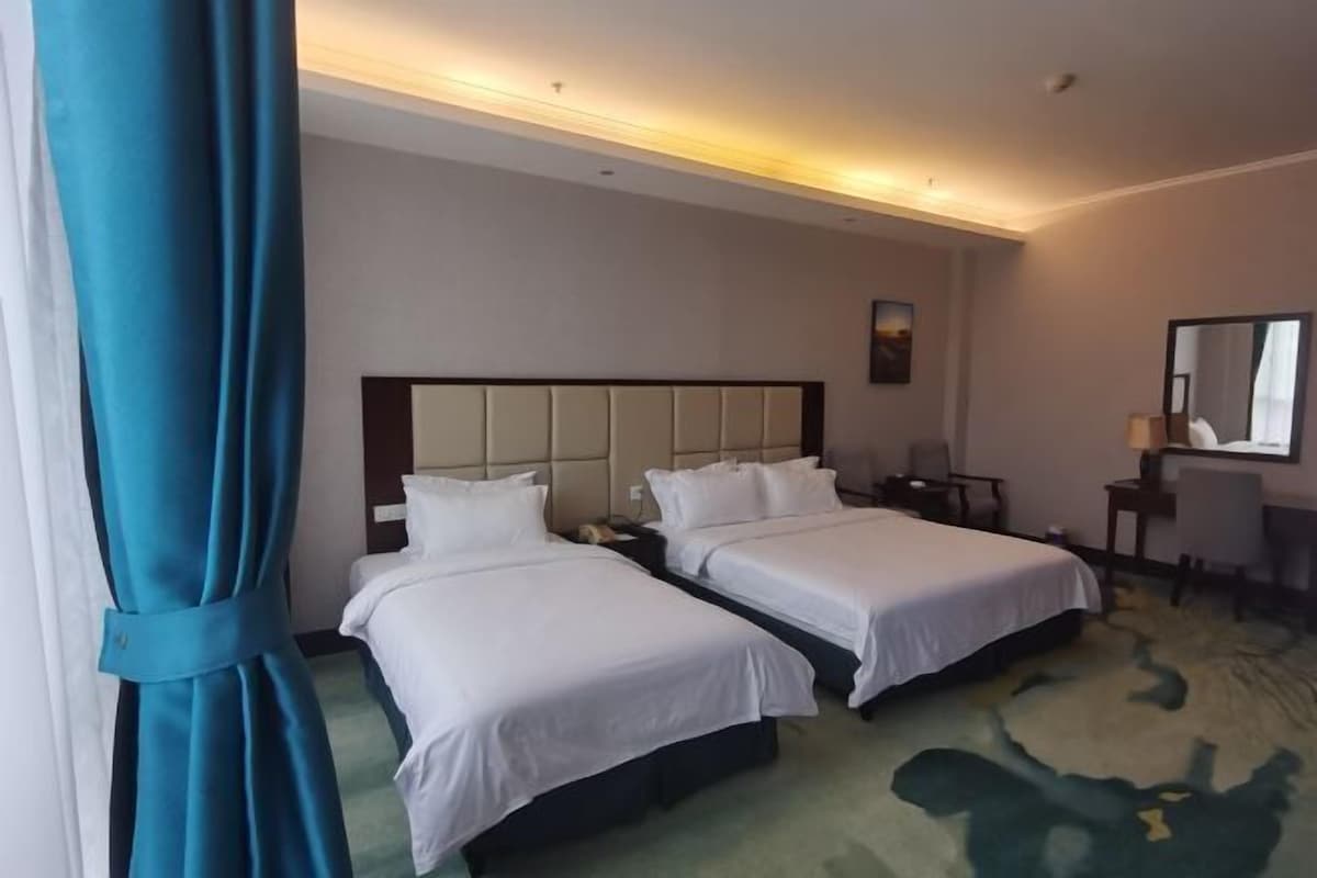 A hotel room with two beds, a desk, a chair, and a large mirror.