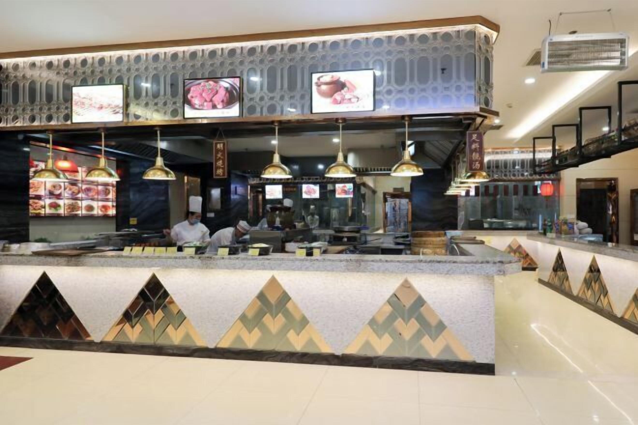 A hotel reception area with a counter, multiple hanging pendant lights, and a decorative wall with geometric patterns.