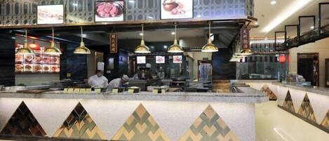 A hotel reception area with a counter, multiple hanging pendant lights, and a decorative wall with geometric patterns.