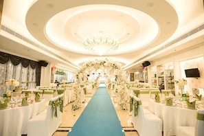 A hotel corridor with a blue carpet, white tables, and chairs, leading to a reception area with a chandelier. - Daxing Hotel (Zhongshan)