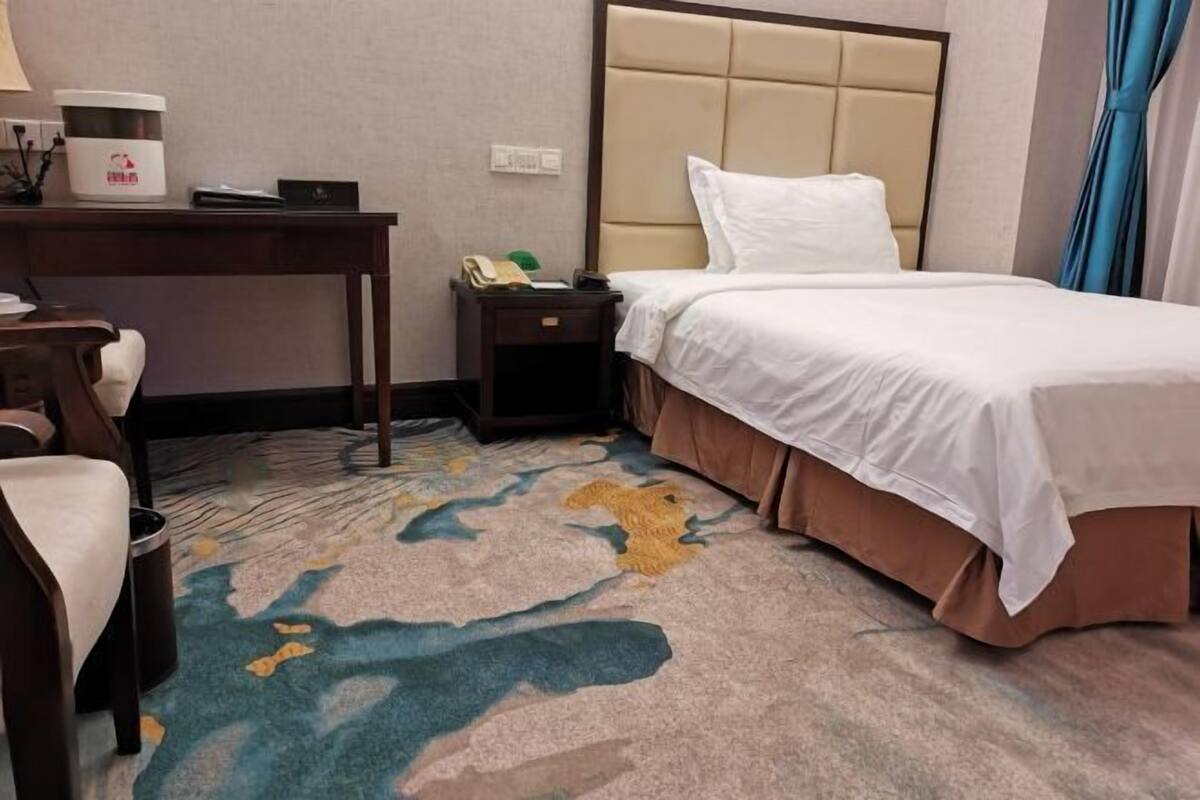 A hotel room with a bed, a desk, a chair, a nightstand, and a carpet with a map design.
