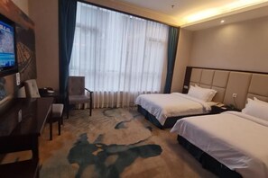 A hotel room with two beds, a desk, a chair, and a large window with curtains.