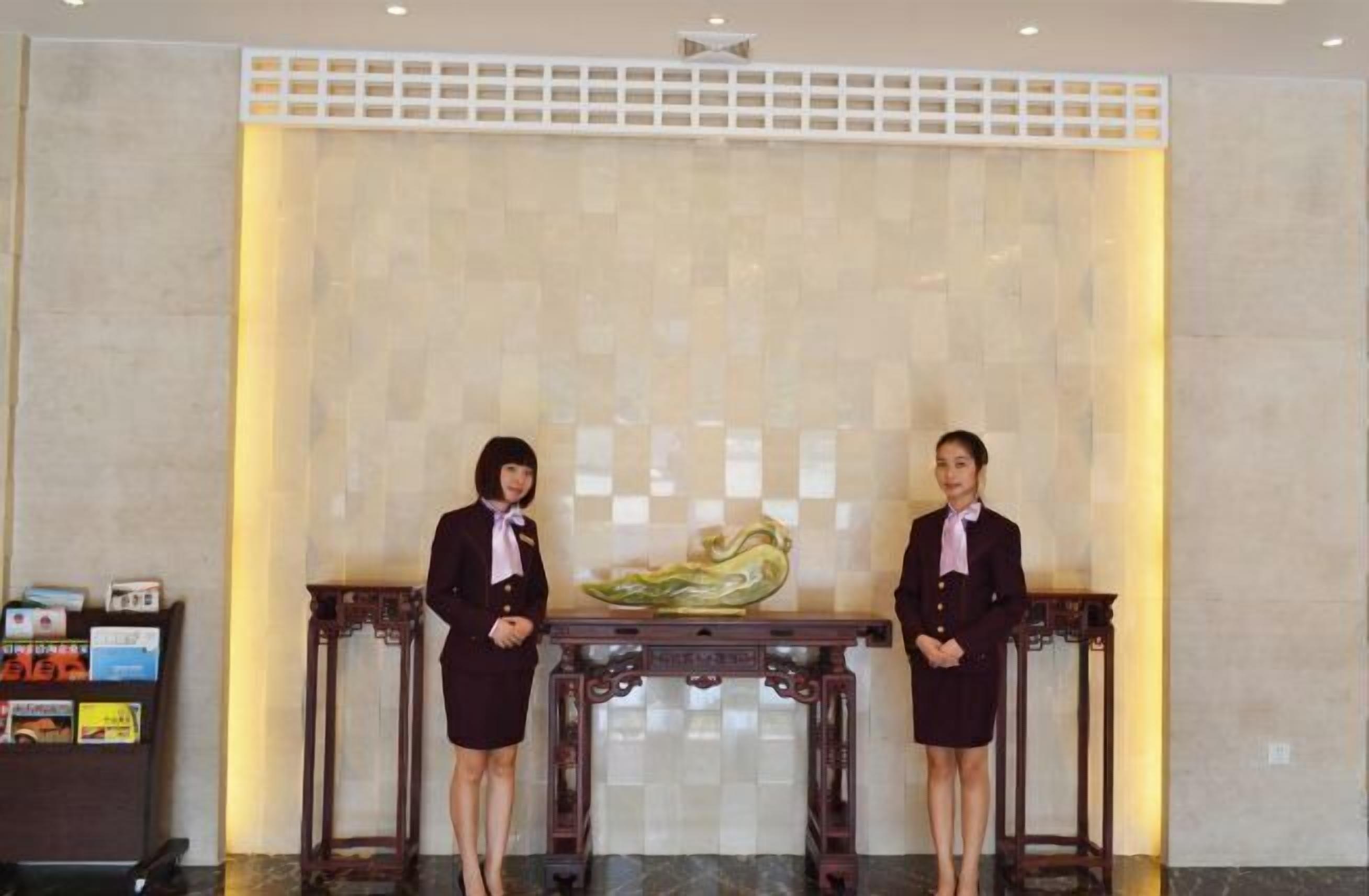 Two receptionists standing in front of a reception desk with a decorative vase.