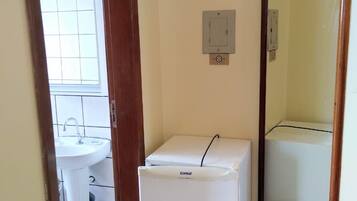 A compact room with a white refrigerator, a small sink, and a mirror.