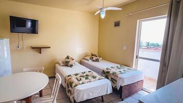 A room with two beds, a TV, a ceiling fan, a table, and a window with curtains.