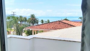 A balcony with a view of a coastal area, including palm trees and buildings with red-tiled roofs. - Pousada Vó Regina (Florianópolis)