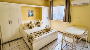 A room with a bed, a small table with chairs, a window with curtains, and an air conditioning unit. - Pousada Vó Regina (Florianópolis)