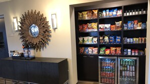 Een snackbar met diverse houdbare snacks en dranken, een koffieapparaat en een decoratieve wandklok.