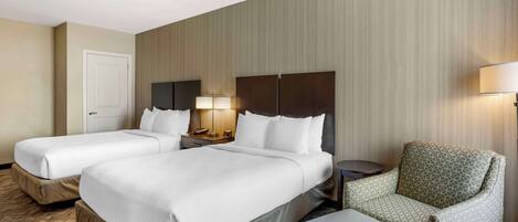 A hotel room with two beds, a chair, a small table, and a lamp.