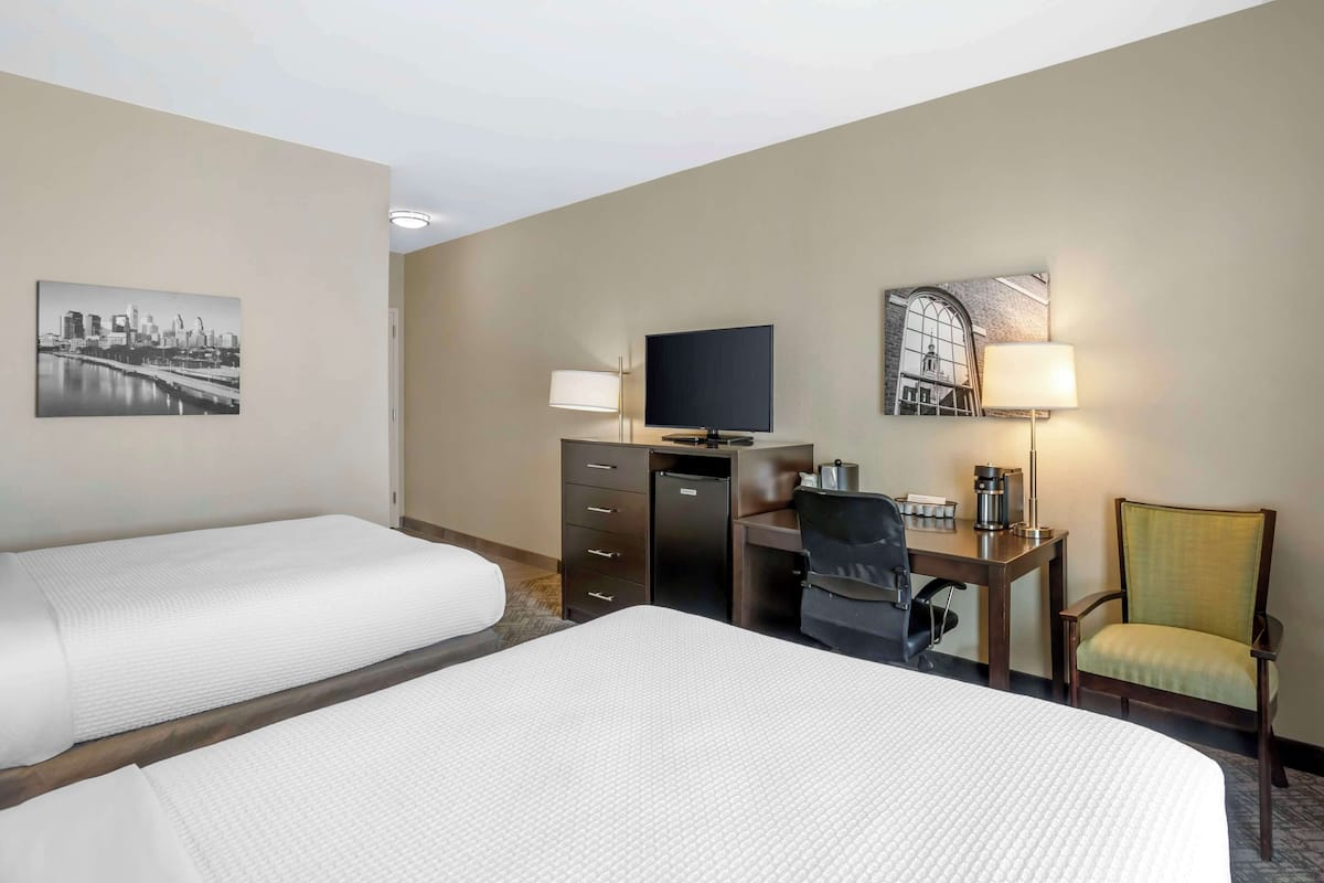 Une chambre d’hôtel avec deux lits, un bureau avec un ordinateur, une télévision et une chaise.