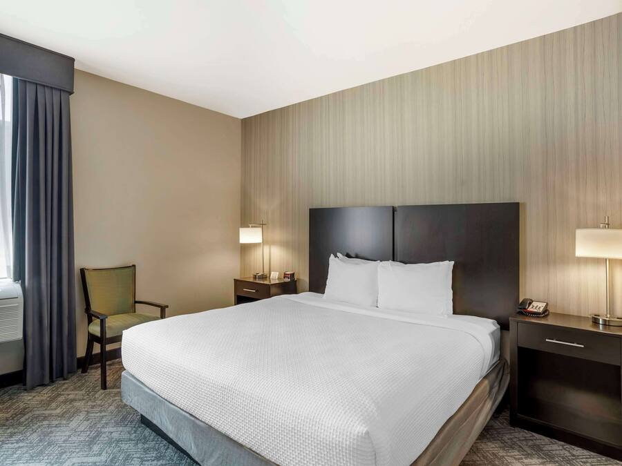 Habitación de hotel con una cama grande, una silla, un escritorio con lámpara y un televisor instalado en la pared.