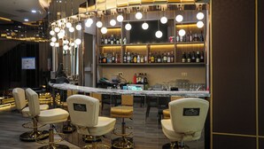 A bar area with multiple bar stools, a marble counter, and a variety of bottles on shelves. - Best Western Premier Batumi (Batumi)