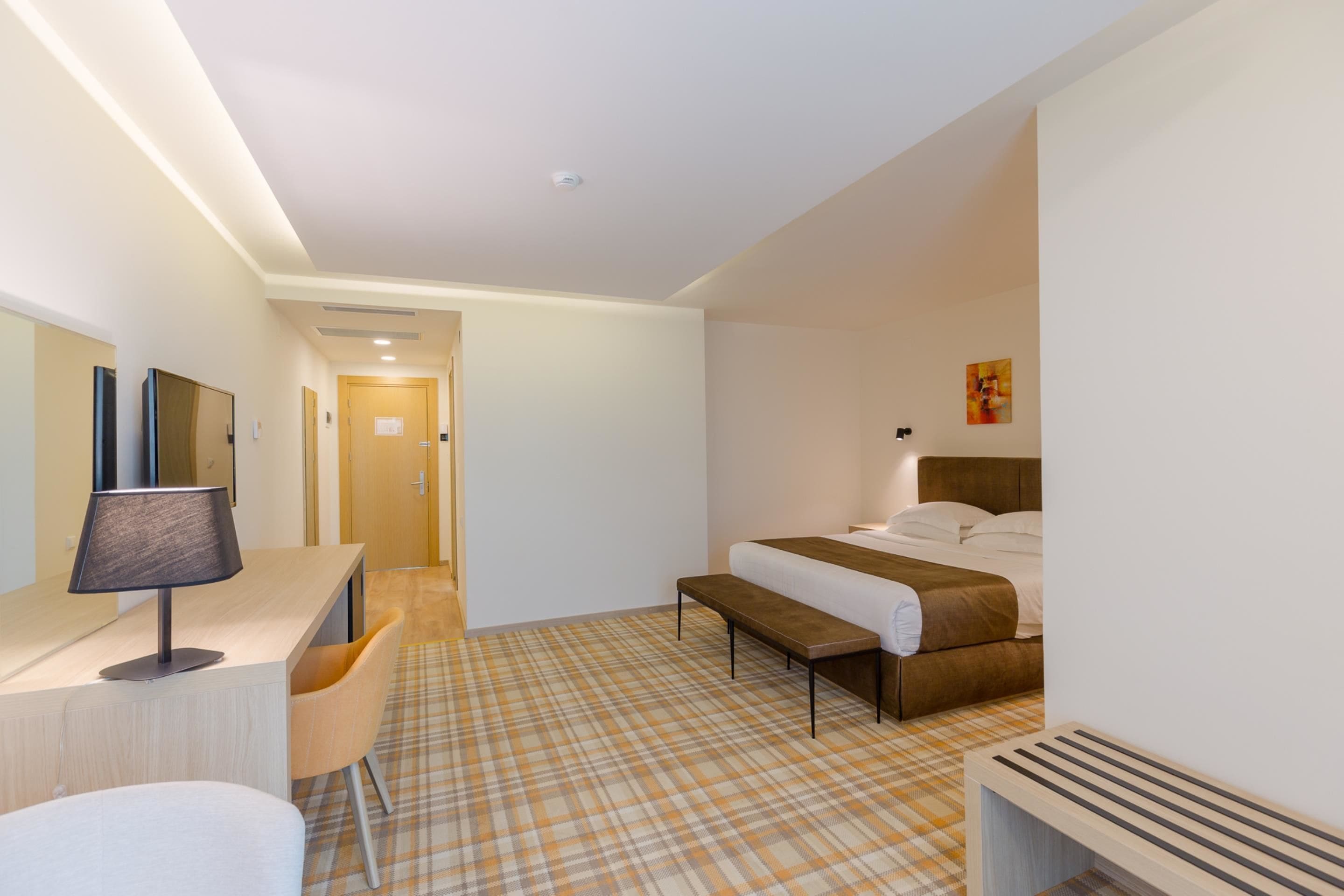 Una habitación de hotel con cama, mesita de noche, lámpara, sillón y recepción.