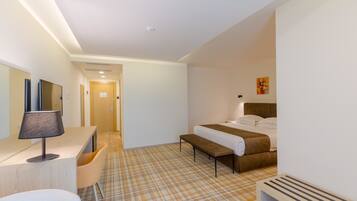 Una habitación de hotel con cama, mesita de noche, lámpara, sillón y recepción.