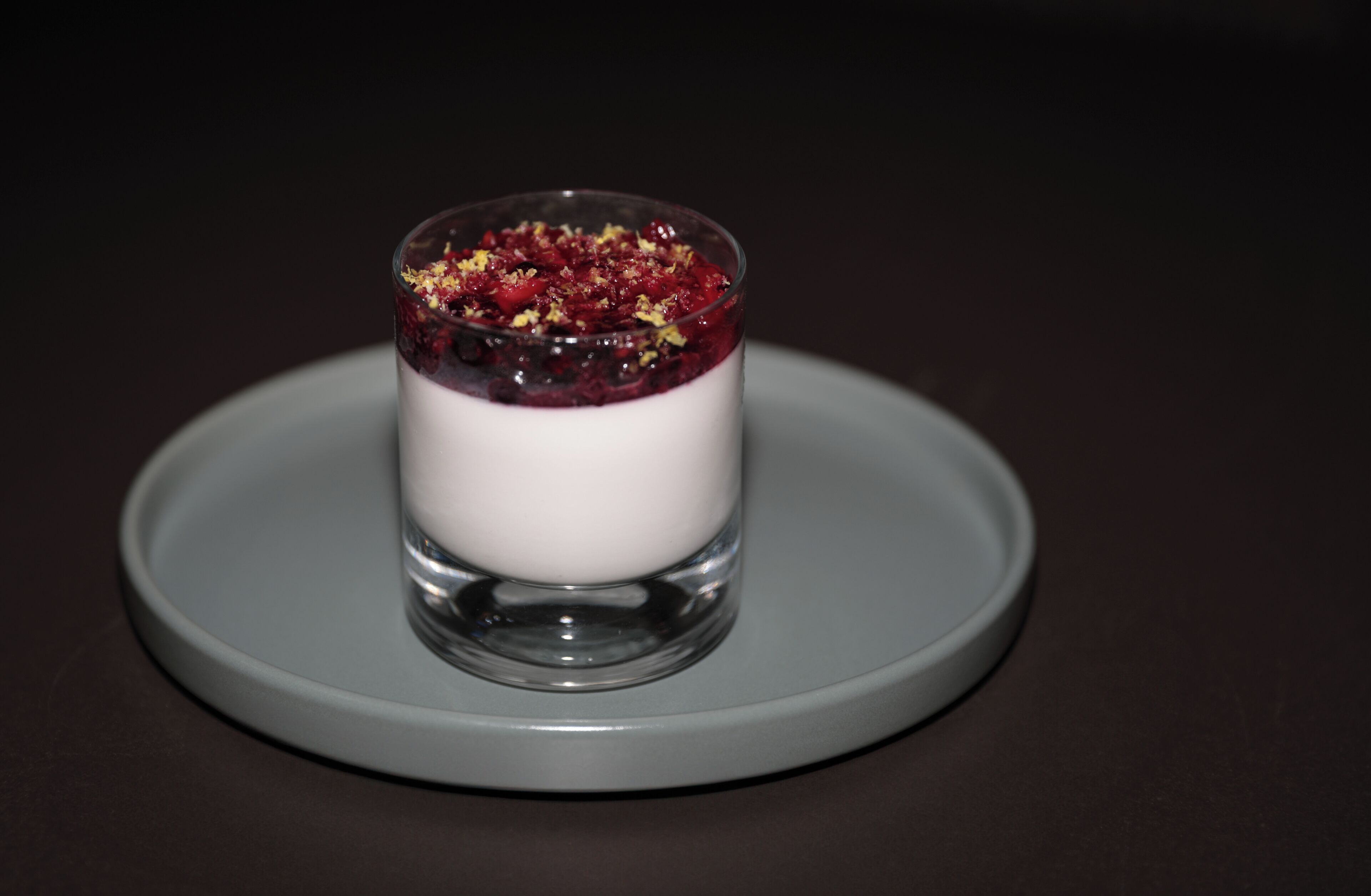 A dessert in a clear glass on a grey plate.