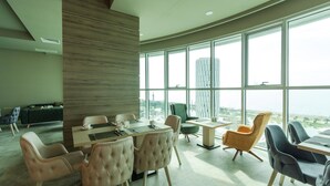A modern dining area with a large window, a high ceiling, and a view of a cityscape. - Best Western Premier Batumi (Batumi)