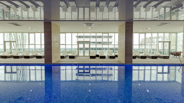 A modern indoor swimming pool with clear blue water, sun loungers, and large windows offering views of the city. - Best Western Premier Batumi (Batumi)