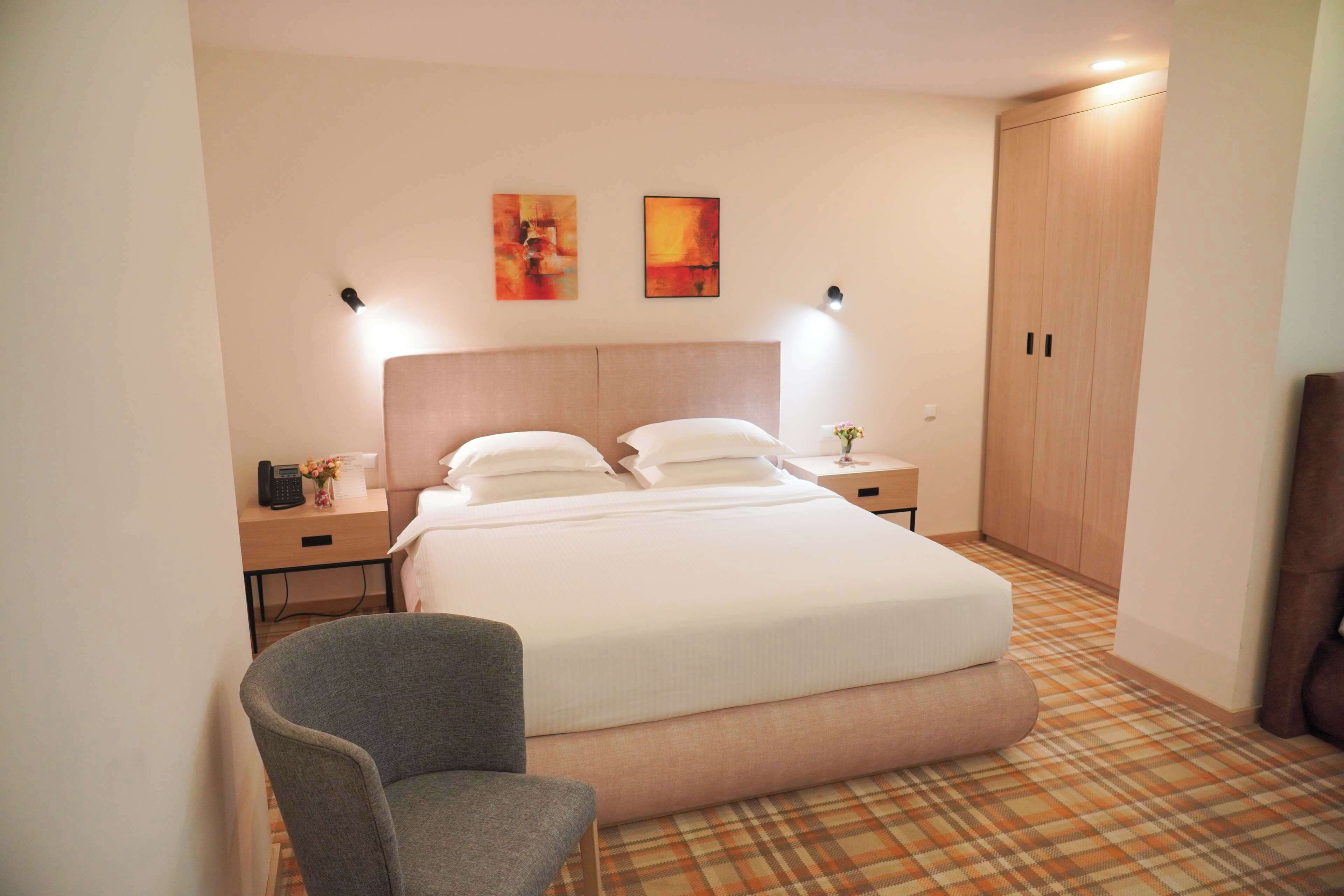 Una camera d'albergo con un letto, due comodini, una sedia, un armadio e due luci a parete.