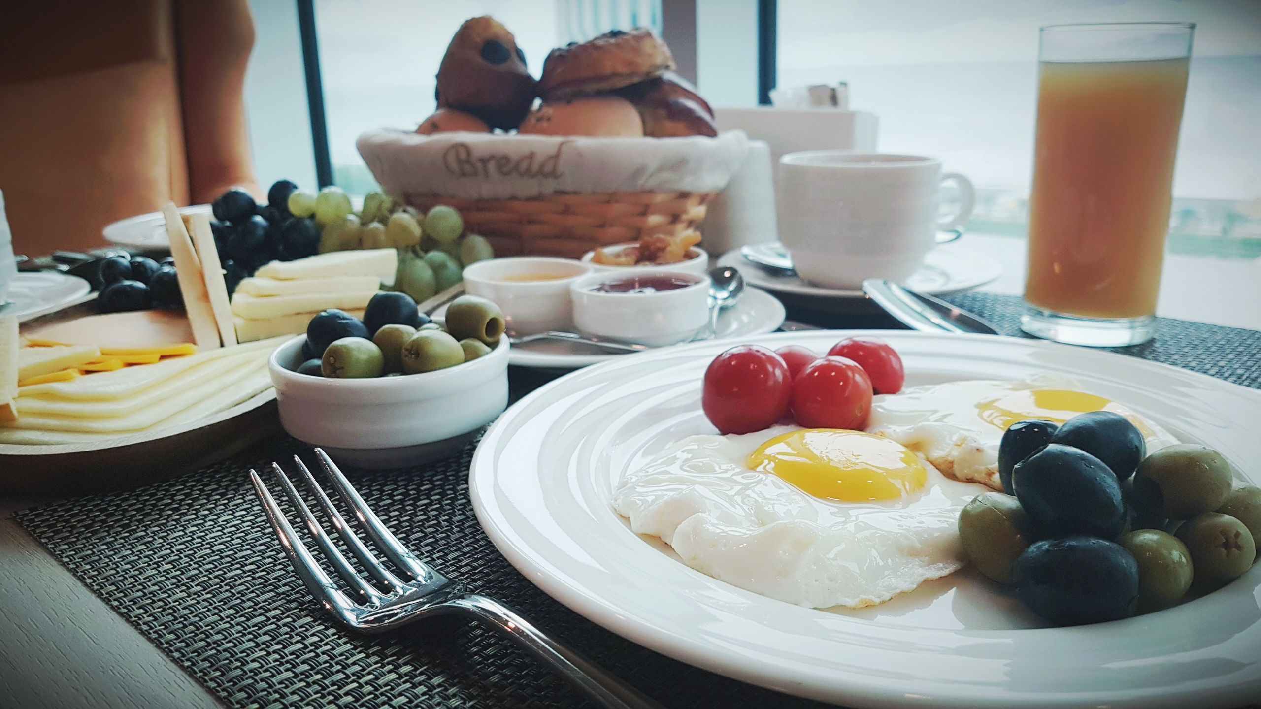 Un desayuno con huevos, aceitunas, tomates, pan y un vaso de jugo.