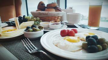Un desayuno con huevos, aceitunas, tomates, pan y un vaso de jugo.