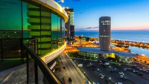 A modern hotel with a curved glass facade, a parking lot, and a view of the sea and city skyline. - Best Western Premier Batumi (Batumi)