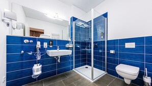 Un baño moderno con paredes de azulejos azules, cabina de ducha de vidrio, lavamanos y retrete.