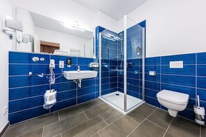 A modern bathroom with blue tiled walls, a glass shower enclosure, a sink, and a toilet. - Best Western Plus Royal Suites (Leipzig)