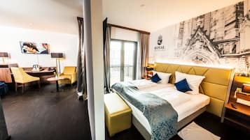 Quarto de hotel com cama, escrivaninha, cadeira, sofá e uma janela grande.