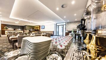 Ein Hotel-Speisesaal mit gedeckten Tischen, eine Bar und Blick ins Freie.