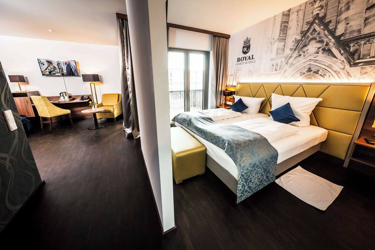 A hotel room with a large bed, a desk with a chair, a sofa, and a TV on the wall.