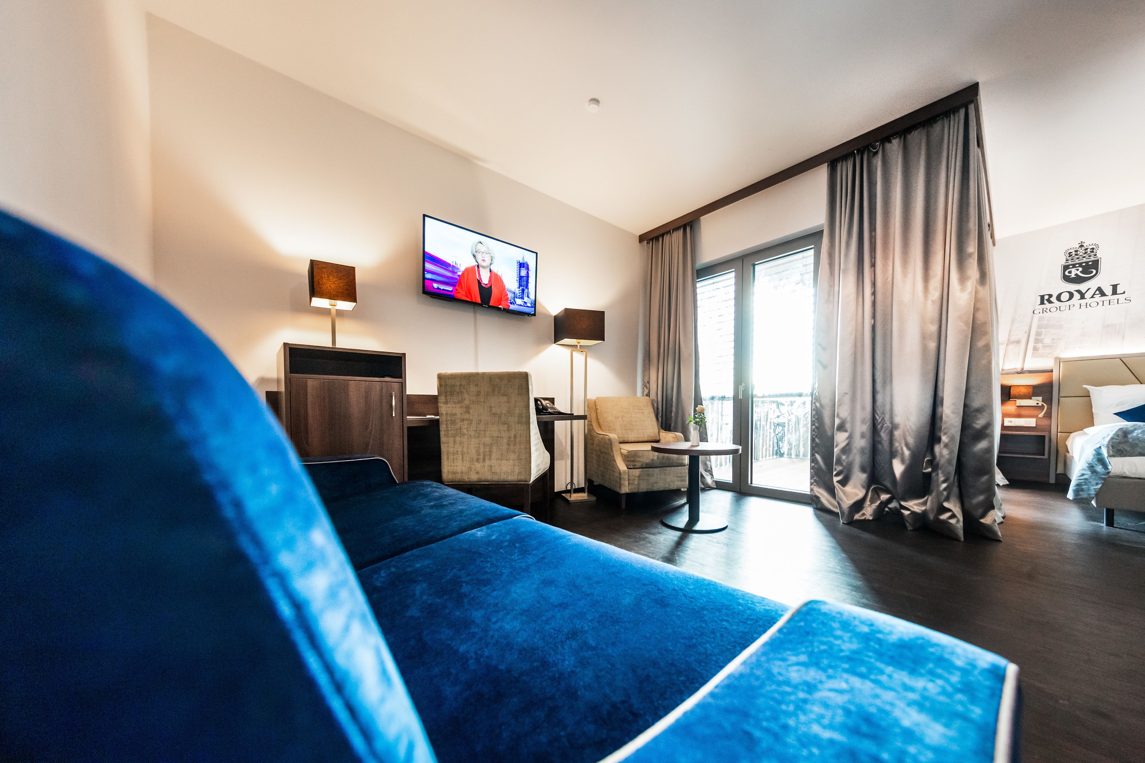 A hotel room with a large bed, a TV, a desk, and a chair.