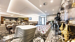 A hotel restaurant with a long dining table set for a banquet, a bar area with various bottles, and a modern interior design.