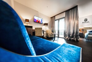 A hotel room with a large blue sofa, a television, a small table, and a bed. - Best Western Plus Royal Suites (Leipzig)