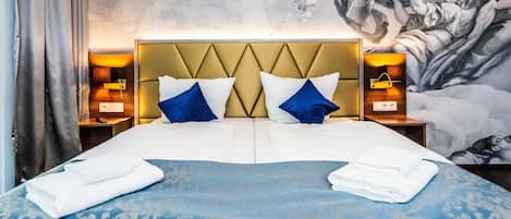 Quarto de hotel com uma cama grande, duas mesas de cabeceira e um mural na parede.