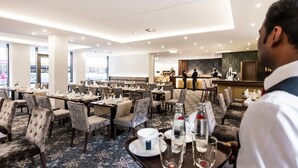 A hotel dining area with tables set for guests, a reception desk, and a view of the street outside. - Best Western Plus Royal Suites (Leipzig)