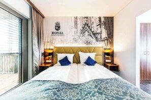 A hotel room with a large bed, a headboard with a crest logo, and a balcony with curtains. - Best Western Plus Royal Suites (Leipzig)