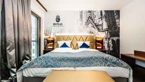 Una habitación de hotel con una cama grande, un cabecero con el logotipo de un escudo y un mural en la pared.