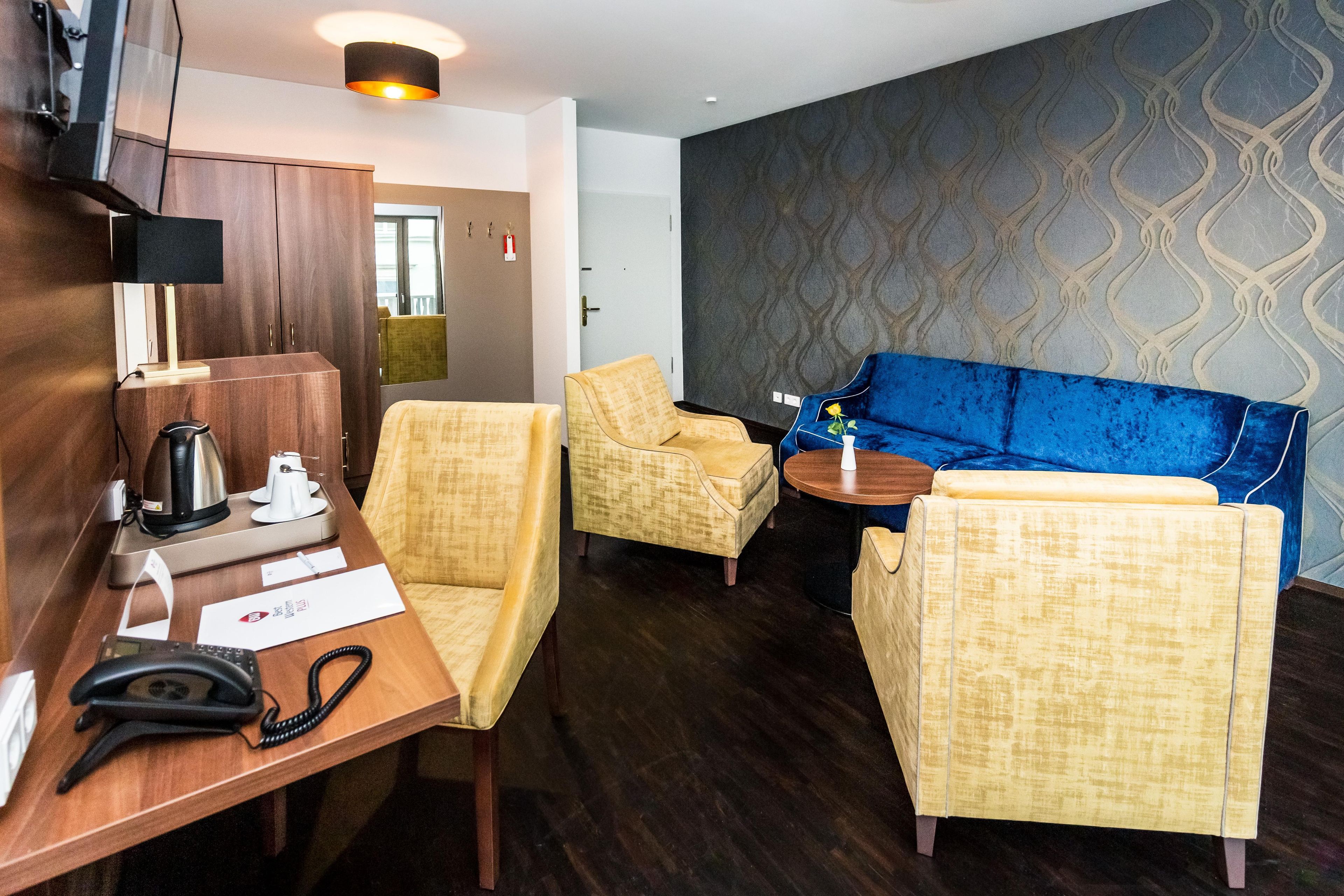 Een hotelkamer met een houten bureau, een telefoon, een koffiezetapparaat en een blauwe bank.