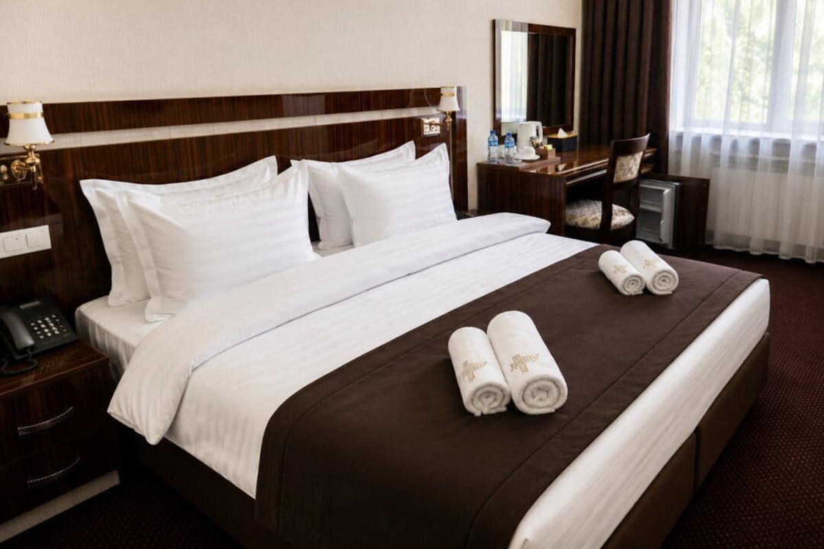 Habitación de hotel con una cama grande, una mesita de noche con teléfono, un escritorio con silla y una ventana con cortinas.
