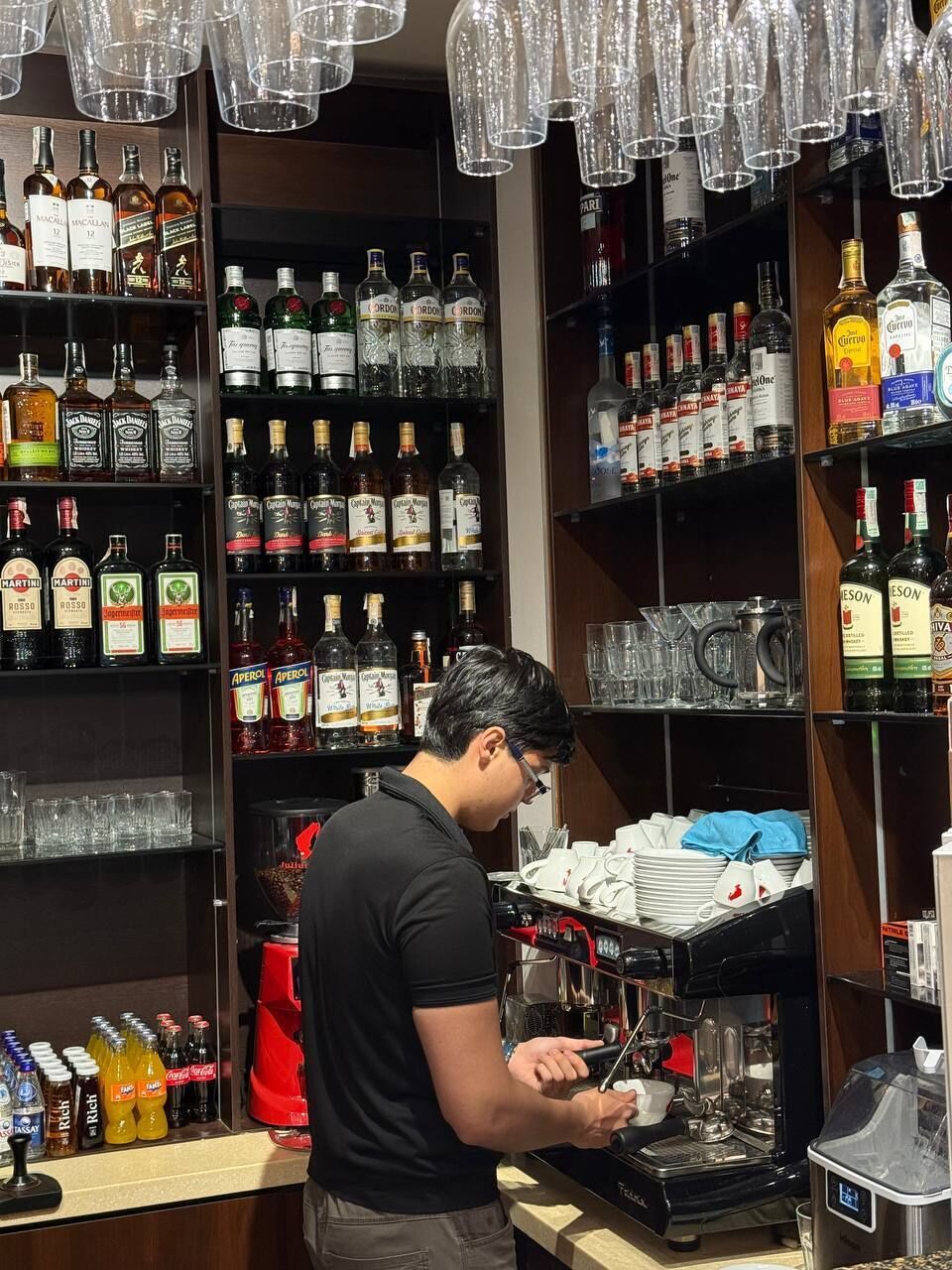A bar area with shelves stocked with various liquor bottles, a coffee machine, and hanging glassware.