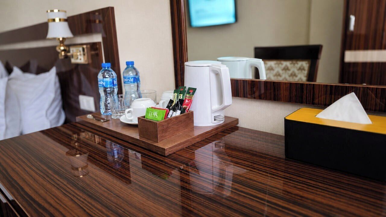 Habitación de hotel con escritorio de madera, cafetera, caja de pañuelos y espejo.