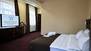A hotel room with a bed, a TV on a dresser, and a sign indicating the hotel name. - Grand Capital Hotel (Tashkent)