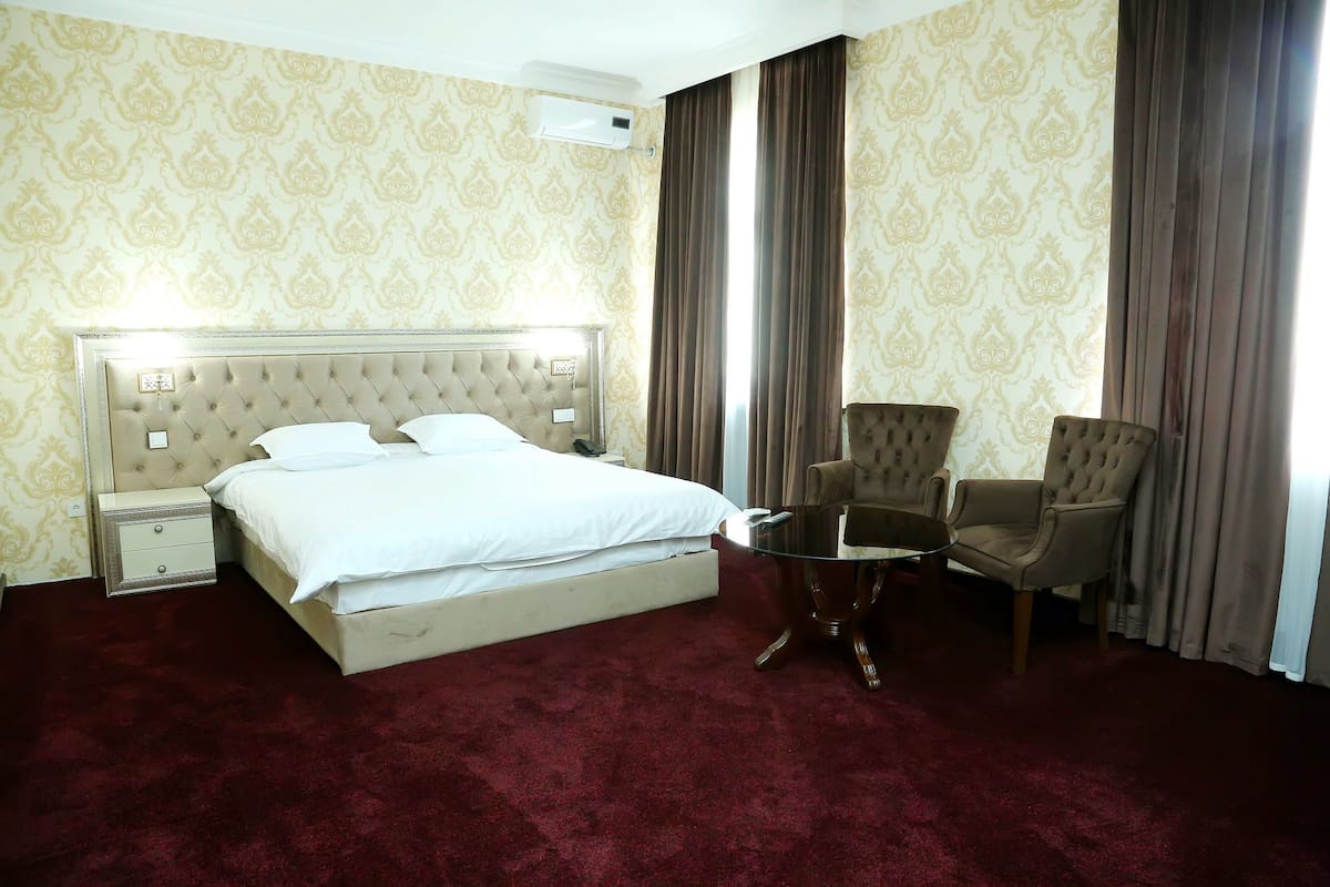 A hotel room with a large bed, two armchairs, a small table, and a nightstand.